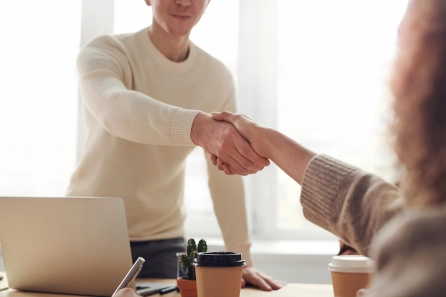 Zwei Personen schütteln sich in einem professionellen Umfeld die Hände und symbolisieren damit eine Win-Win-Situation im Coaching, in der beide Seiten profitieren und positive Ergebnisse für Coach und Klient erzielt werden.