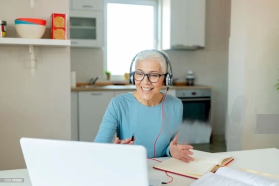 Eine lächelnde ältere Frau, die eine Online-Coaching-Sitzung von zu Hause aus durchführt, ein Headset trägt und sich mit einem Kunden unterhält, symbolisiert die positive Wirkung und den Wandel, den Coaches bewirken.