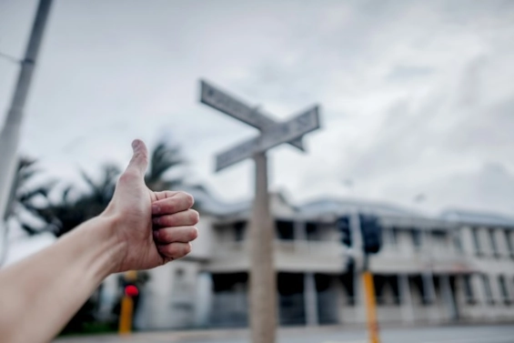Daumen-nach-oben-Geste in der Nähe eines Wegweisers an einer Kreuzung, als Symbol für Orientierung, Richtung und die positive Wirkung von Coaching bei der Entscheidungsfindung und der Bewältigung von Herausforderungen.